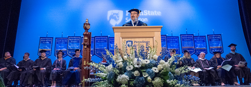 Penn State Scranton chancellor, wearing cap and gown, standing at podium at graduation ceremony