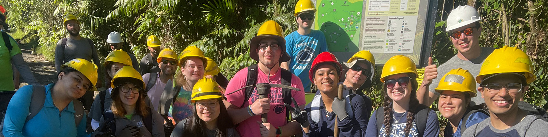 group of fifteen volunteer students wear yellow hard hats while they do volunteer work