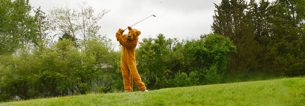 nittany lion mascot hitting a golf ball off a tee on a green grassy golf course