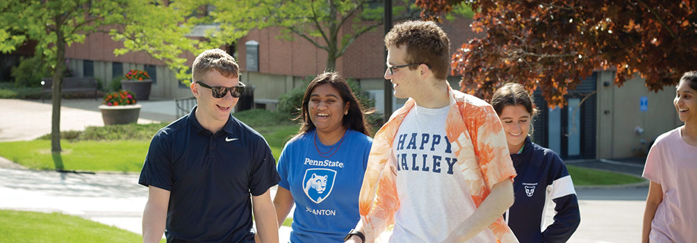 5 smiling students walking across campus