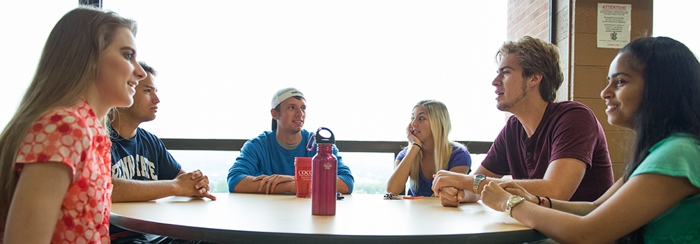 six diverse first year students sit at table in cafe