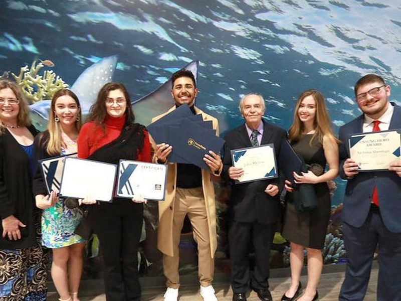 group of students pose in front of aquarium holding their award certificates