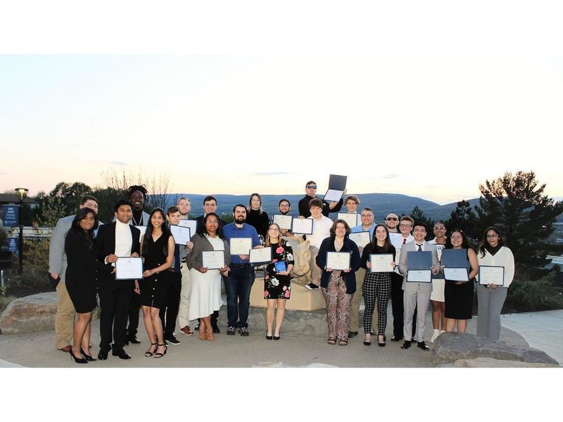 group of student award winners pose for photo at campus lion shrine at sunset