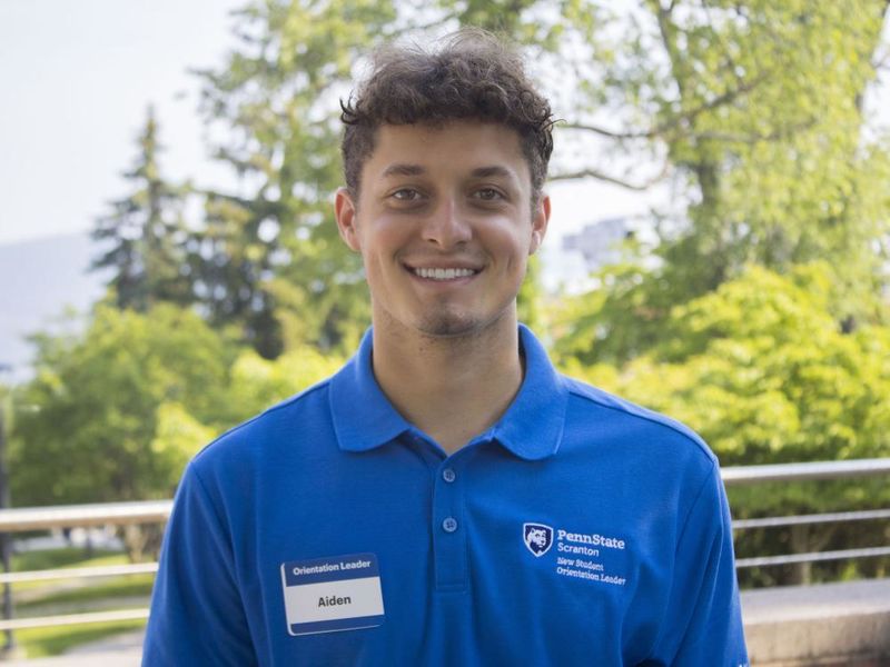Student wearing a shirt that reads 'New Student Orientation' smiles for photo