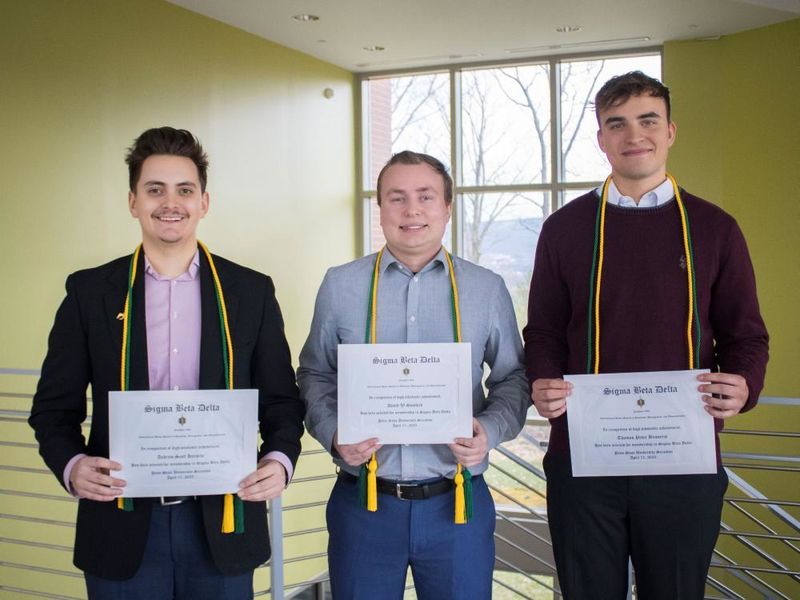three students show off their honor society certificates, cords and pins