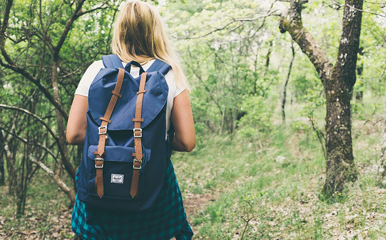 teen girl walking in woods with a backpack on