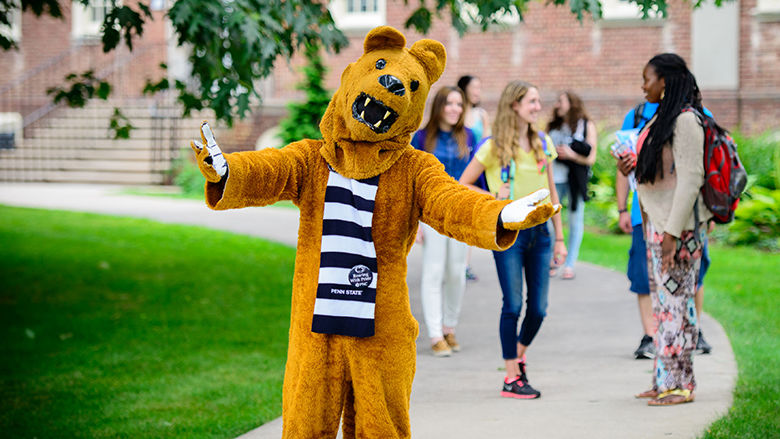 lion mascot on campus sidewalk, with arms stretched out in a welcoming way