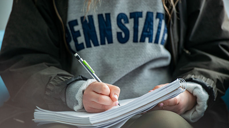 close up of a student wearing penn state shirt and writing in a notebook
