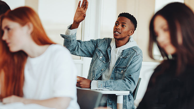 smiling student in class raises his hand to answer a question
