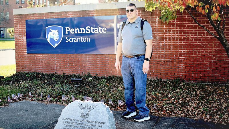 Jayson Zimmerman poses for a photo at entrance to Scranton Campus near veterans marker