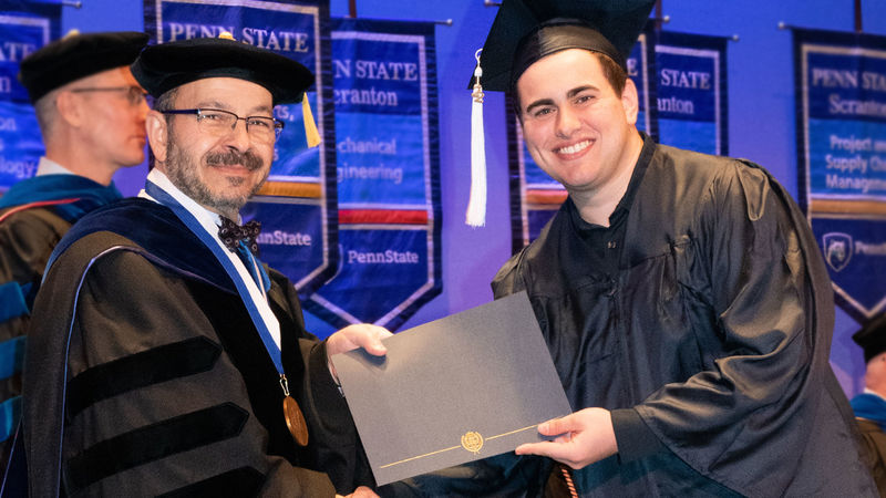 smiling graduate in cap and gown receives diploma from chancellor