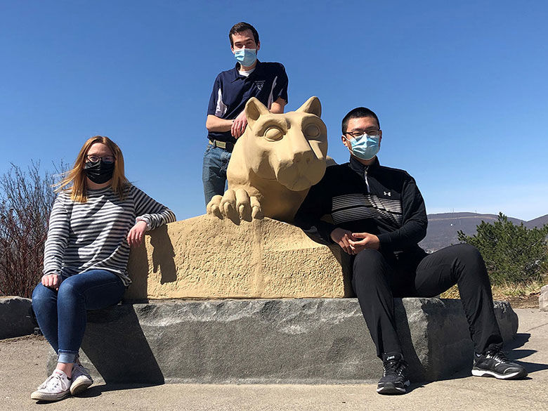 3 students wearing masks sitting by the lion shrine statue