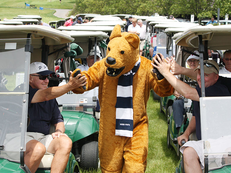 Lion mascot walking between two rows of golf carts driven by golfers