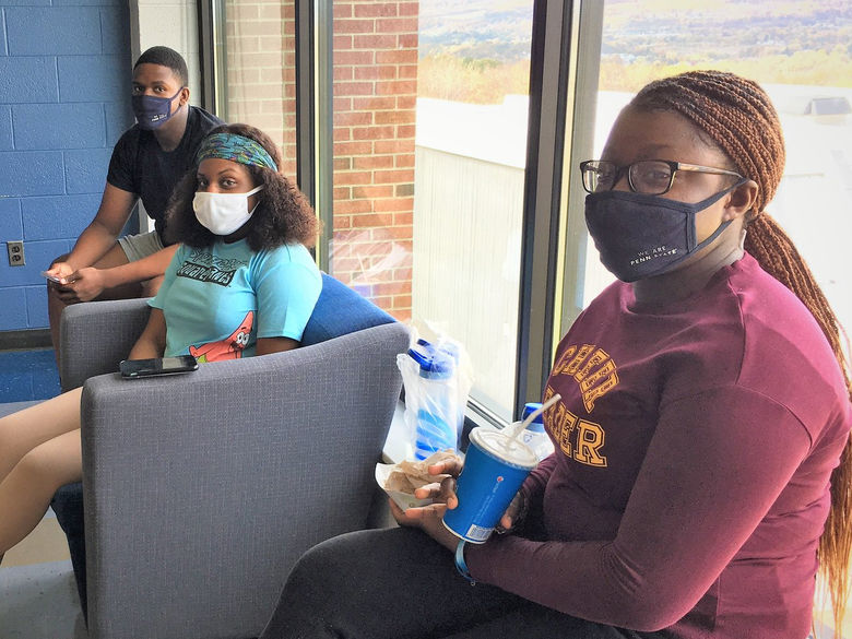 three students wearing protective mask sit 6 feet apart