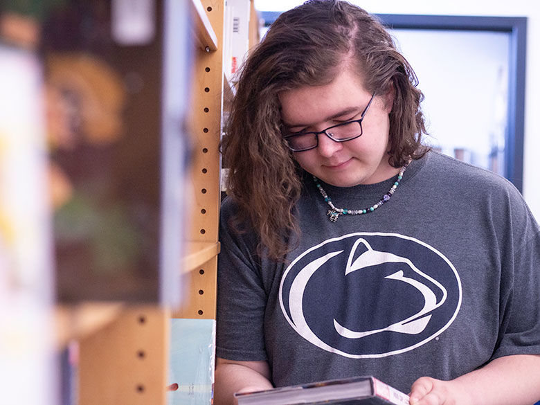 student wearing a penn state tee looks at a book in the library