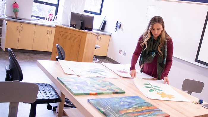 Lecturer in Art, Corianne Thompson stands at large art table in an art studio and looks at student artwork