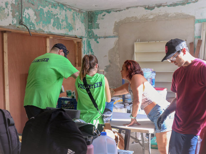 group of student volunteers painting inside damaged house