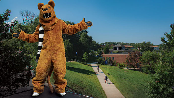 lion with arms stretched out stands overlooking a green campus with students walking