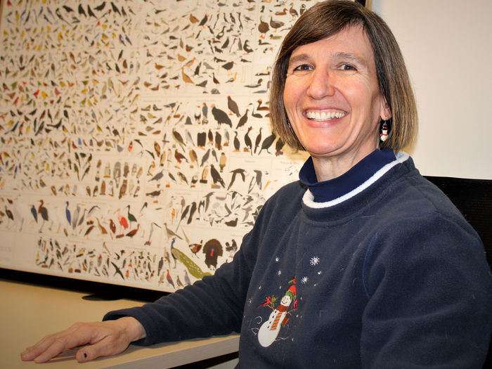 Dr. Meg Hatch seated in front of a chart depicting bird species