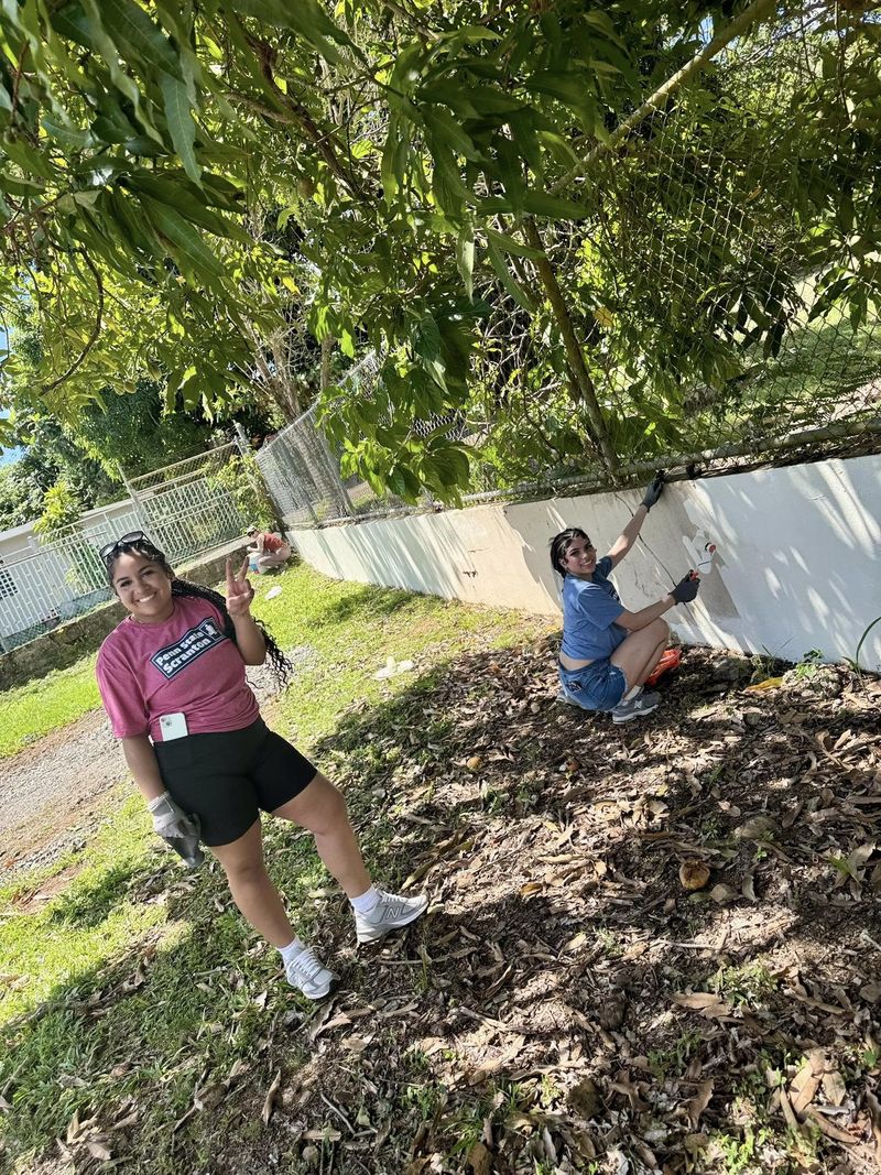 Three female students work on painting an outside garden wall