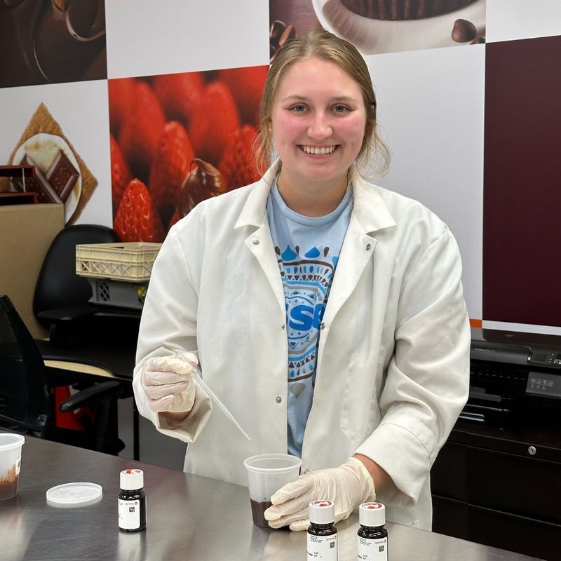 A student wearing a white lab coat holds a beaker and dropper