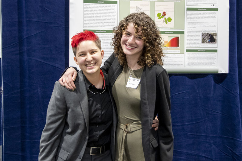 Two students pose in front of a poster about invasive species at the regional symposium