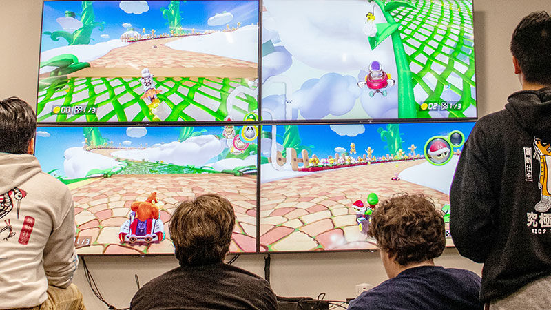 four students play video game on large jumbo tv screens