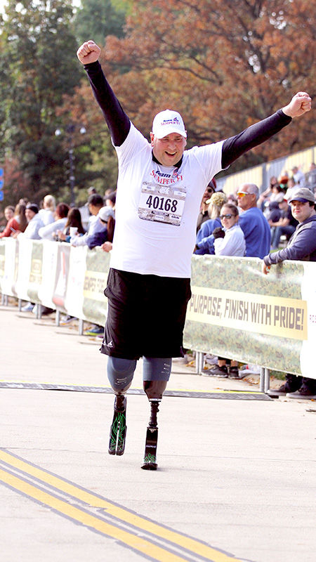 Jayson Zimmerman raises his arms in triumph as he crosses the finish line of the Team Semper Fi 10K marathon