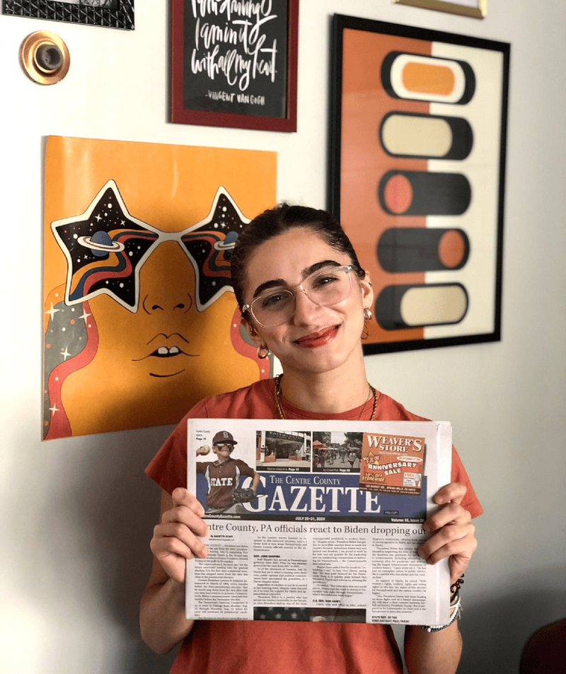 A student wearing glasses holds up an issue of the Gazette newspaper