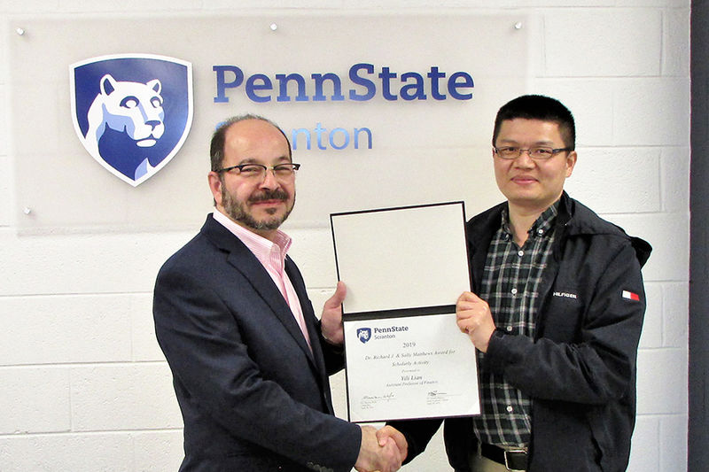 man in suit presents certificate to smiling man