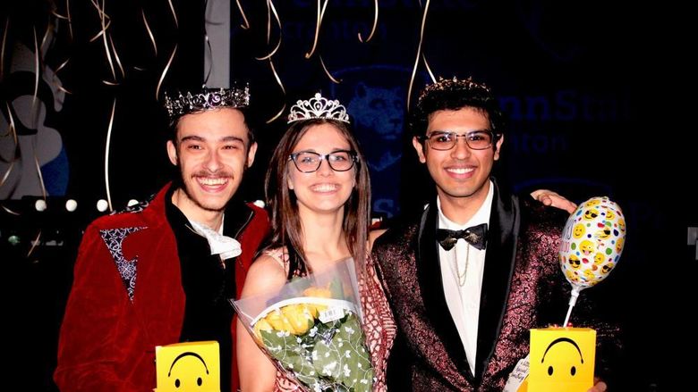 Three Student THON dancers wearing crowns and formal wear and holding yellow flowers pose for a photo after being announced at the THON Prom