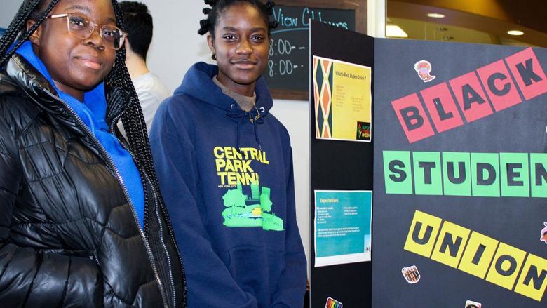 Black student union leaders pose for a photo next to a display promoting their group on campus