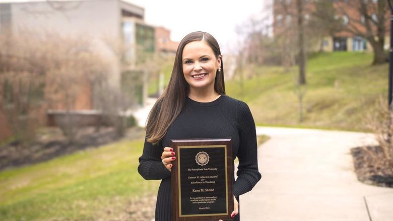 Kara Stone poses outside fo the library building with her award plaque
