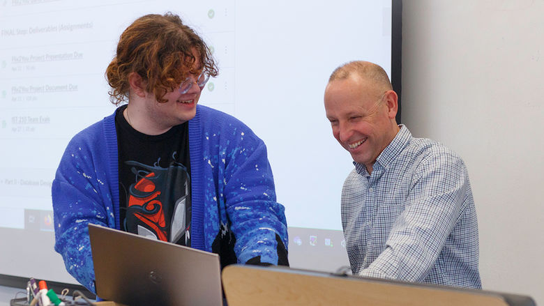 student and teacher share a laugh while reviewing work on a laptop