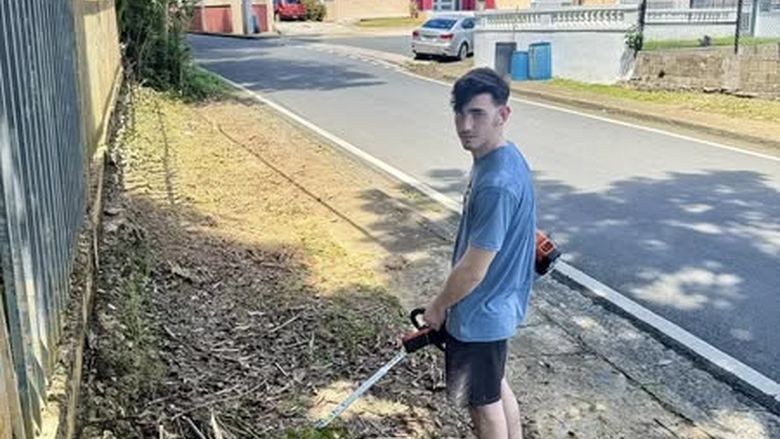 Male student clearing an outside area of overgrown weeds with a weed whacker
