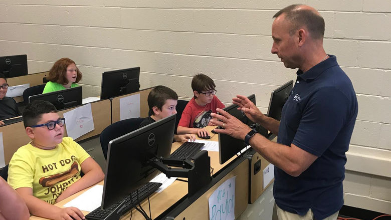 faculty member in front of classroom, young students at computers