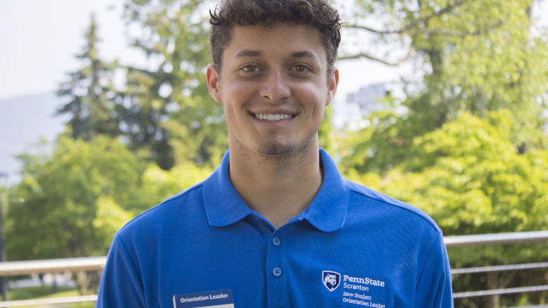 Student wearing a shirt that reads 'New Student Orientation' smiles for photo