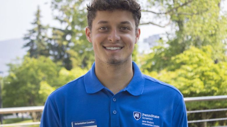 Student wearing a shirt that reads 'New Student Orientation' smiles for photo