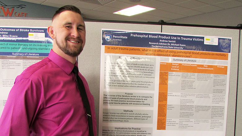 student standing next to poster of research project