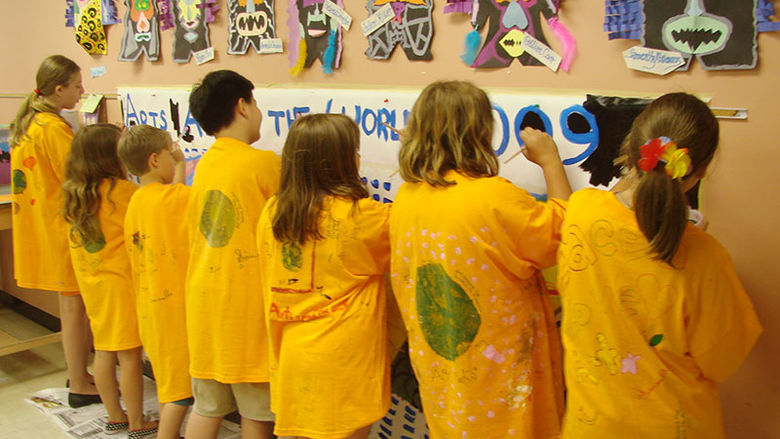 Students in matching yellow camp t-shirts paint a mural on a wall