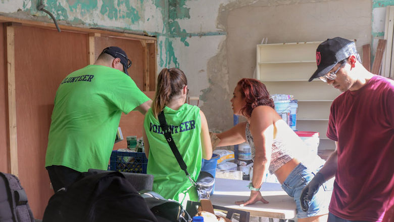 group of student volunteers painting inside damaged house
