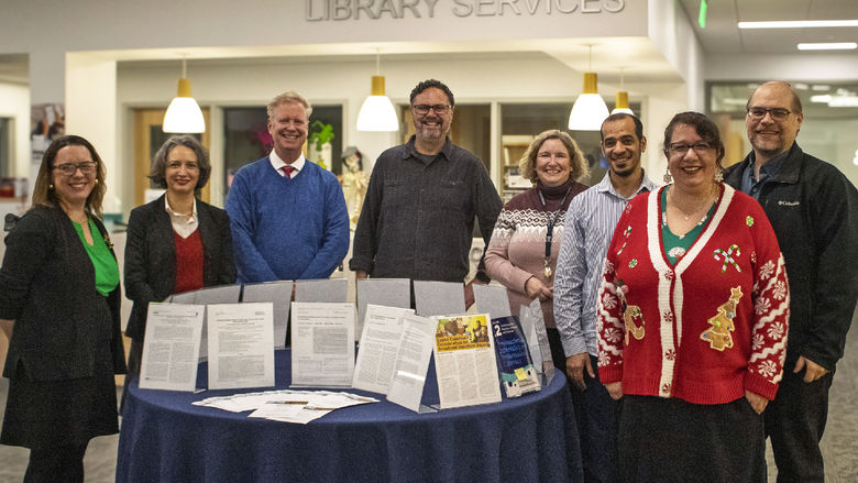 published faculty authors pose for a photo in the campus library near a display of their works