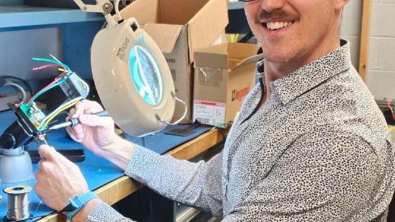 A student smiles for the camera while holding tools to work on a piece of computer hardware