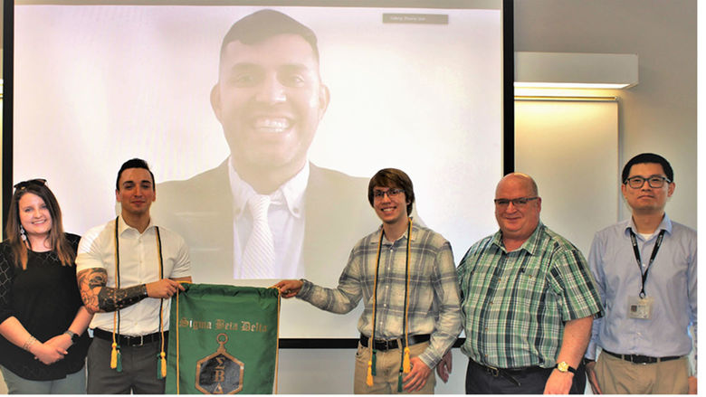 sigma beta delta group posed in front of screen with virtual image of co-inductee Carlos salazar