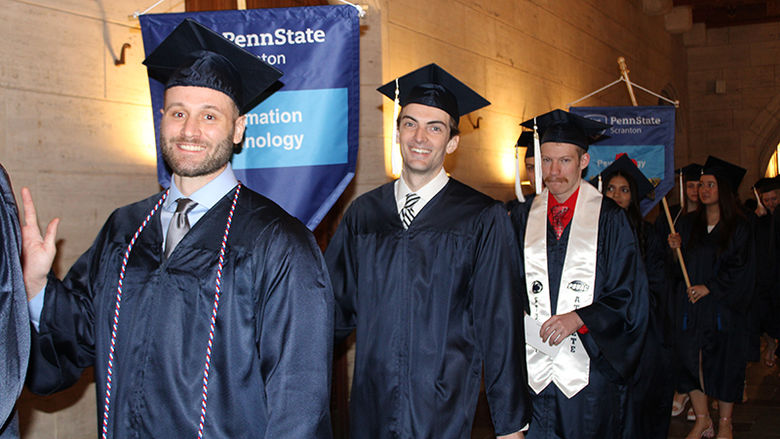 3 men in cap and gown smile at their graduation