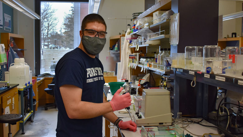 Herne wearing gloves and glasses holds pipette in lab