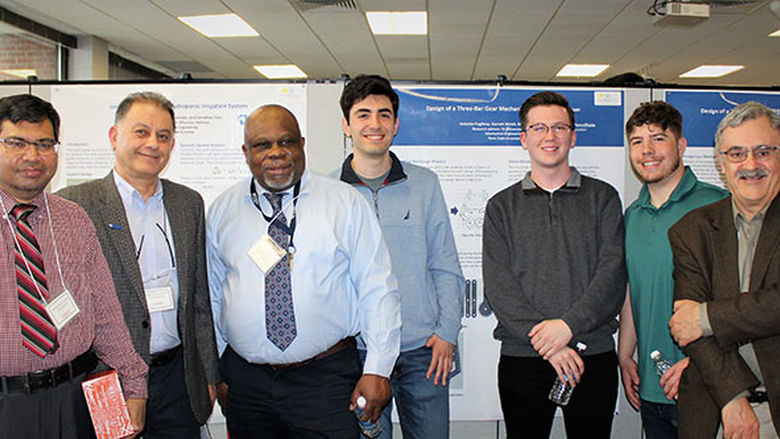 4 faculty pose with 3 students in front of engineering poster presentation at research fair