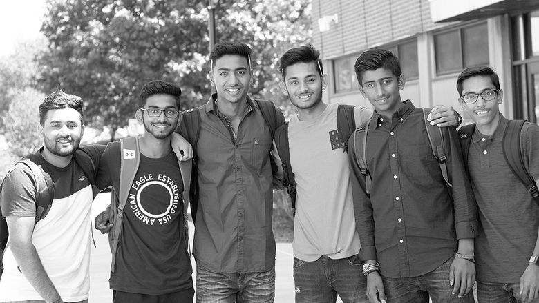 6 students stand arm and arm in front of a brick building