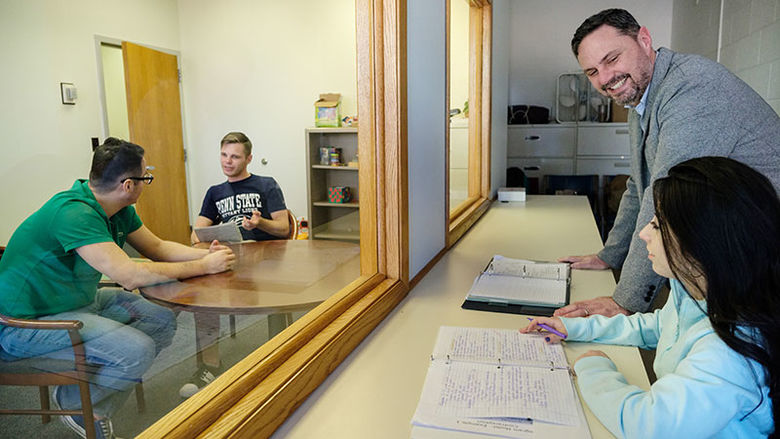 teacher works with a student and two student subjects in an observation window lab