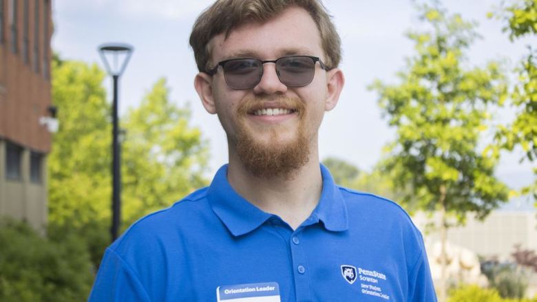 Student with glasses smiling with trees in the background